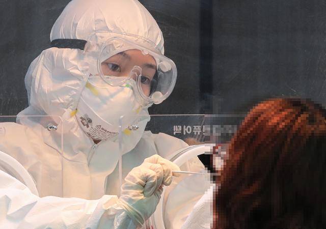 21일 서울 중구 서울역 광장 신종 코로나바이러스 감염증(코로나19) 임시 선별검사소에서 보호복을 입은 검사 담당 관계자가 시민을 검사하고 있다. 연합뉴스