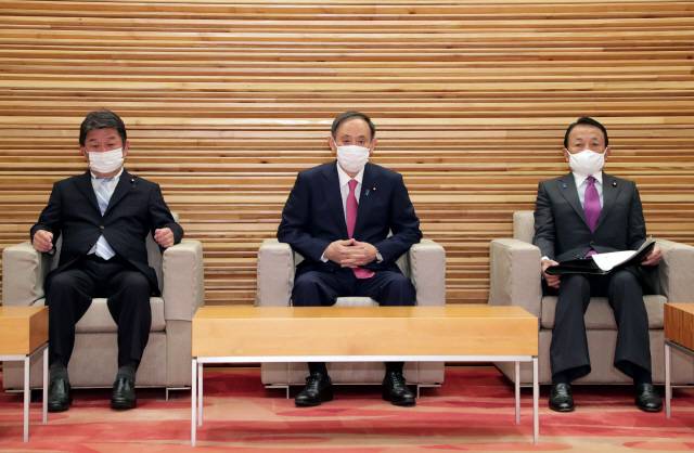 스가 요시히데(가운데) 일본 총리가 22일 도쿄 총리 관저에서 열린 각료 회의에 참석해 모테기 도시미쓰(왼쪽) 외무상, 아소 다로 부총리 겸 재무상과 함께 앉아 있다. 스가 내각은 이날 올림픽 취소 결정 관련 외신 보도를 즉각 부인했다.  /AFP연합뉴스