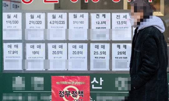 한 시민이 부동산 매물정보와 정부의 부동산 정책을 규탄하는 포스터가 붙은 공인중개업소 앞을 지나가고 있다. <연합뉴스>