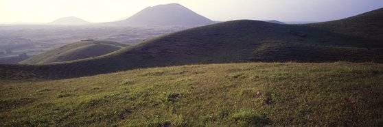 김영갑이 남김 용눈이오름의 현란한 곡선. 능선에 올라 다른 능선을 바라봤다. 능선 너머로 멀리 다랑쉬오름이 보인다. [사진 김영갑갤러리]