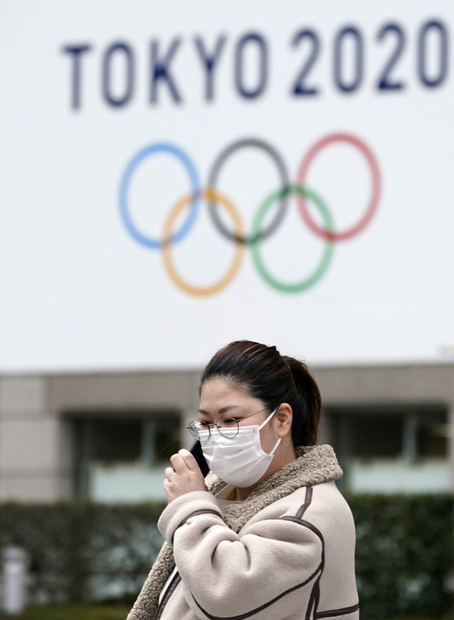 한 일본인 여성이 마스크를 쓴 채 지난 27일 일본 도쿄도 청사의 올림픽 광고 현수막 앞을 지나며 통화하고 있다. 도쿄 | EPA연합뉴스