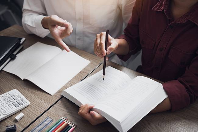 Asian young university students studying together sitting at desk in library.