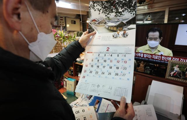 31일 서울 광장시장에서 한 상인이 정부의 거리두기 연장 발표를 TV로 시청하며 2월달 달력을 살펴보고 있다. 뉴스1