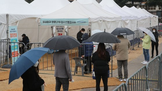 설 연휴 마지막 날인 지난 14일 부산 부산진구 놀이마루 운동장에 설치된 임시 선별검사소에 코로나19 검사를 받으려는 시민들이 우산을 쓴 채 기다리고 있다. 송봉근 기자