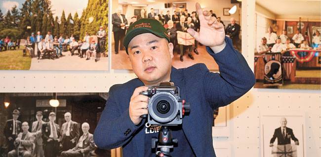 사진작가 라미 현이 서울 관악구 촬영 스튜디오에서 현지 촬영한 참전용사 사진을 배경으로 포즈를 취하고 있다.    신창섭 기자