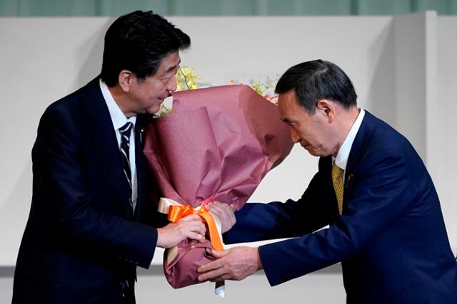 지난해 9월 일본 자민당 총재로 선출된 스가 요시히데(오른쪽) 후보가 당시 총재였던 아베 신조 총리로부터 축하 꽃다발을 받고 있다. 도쿄=AFP 연합뉴스