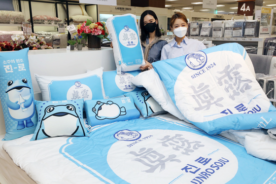 Models hold up bed sheets and pillows with the branding of Hite Jinro soju displayed at Emart’s branch in Seongsu-dong, Seoul on Monday. The products are a collaboration with Nara Home Deco. Food and beverage companies have been increasingly collaborating with fashion companies. [EMART]