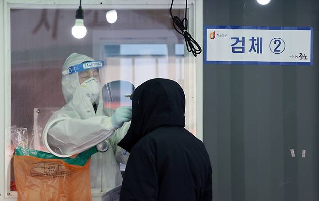 A medical worker takes sample from a person in line for COVID-19 check at a temporary diagnostic center made near Seoul Station on Sunday. (Yonhap)