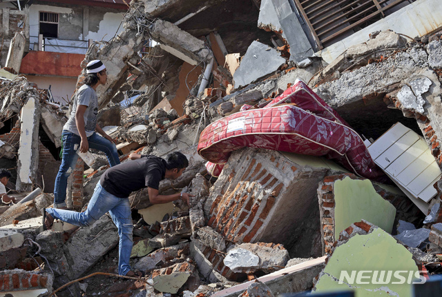 [마무주=AP/뉴시스]18일 인도네시아 웨스트 술라웨시주 마무주 주민들이 지난 15일 발생한 지진으로 무너진 건물을 살피고 있다. 이번 지진으로 80여 명이 숨지고 600여 명이 다친 가운데 구조대는 수색 작업을 이어가고 있으며 피해 주민들에게 구호품이 도착하고 있다. 2021.01.18.