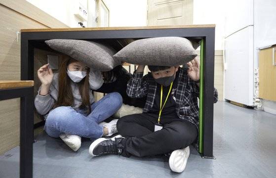 지진 체험에 나선 소중 학생기자단이 식탁 밑으로 들어가 엉덩이는 바닥에 딱 붙여 앉고, 몸을 웅크리며 방석으로 머리를 보호하면서 흔들림이 멈출 때까지 기다리고 있다.