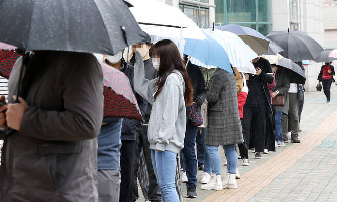 12일 오후 서울 중랑구 보건소에 마련된 코로나19 임시선별진료소를 찾은 시민들이 우산을 쓰고 순서를 기다리고 있다. 연합뉴스