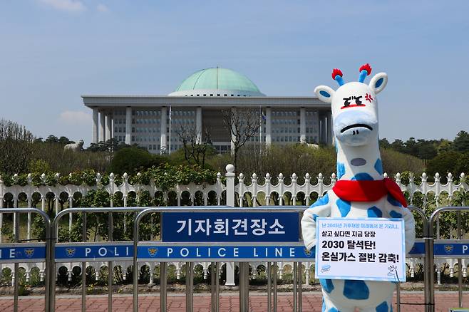 Kirini the blue-spotted giraffe holds up a sign in front of the National Assembly in southwestern Seoul. It reads, “2030 coal phaseout! Cut greenhouse gas emissions in half!” (Korea Beyond Coal)