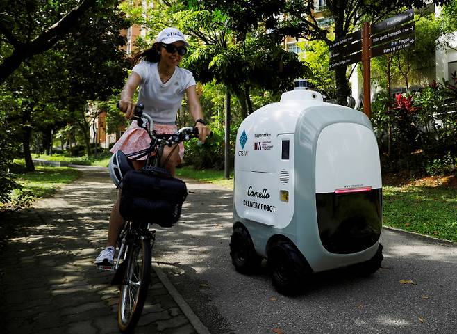지난 4월 6일(현지시간) 싱가포르에서 한 시민이 식료품을 배달하는 자율주행 배달로봇 옆을 자전거를 타고 지나가고 있다.  / 로이터연합뉴스