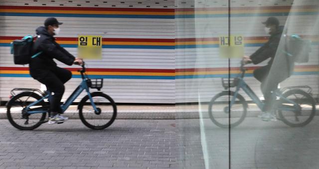 한 온라인 플랫폼 업체 배달기사가 지난달 29일 배달음식 가방을 멘 채 자전거를 타고 서울 중구의 한 폐업 상가 앞을 지나고 있다. 뉴스1
