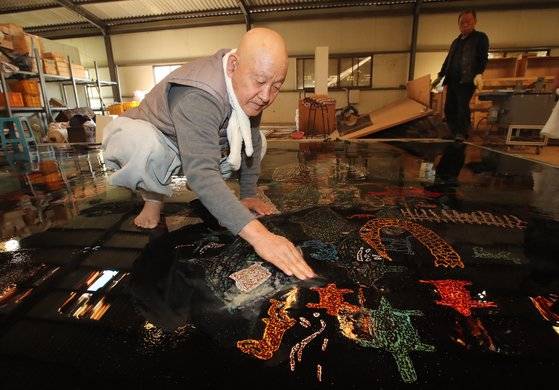 성파 스님이 맨발로 올라가 반구대 암각화를 옻칠로 되살린 작품을 손으로 닦고 있다.