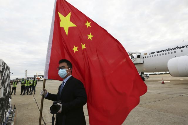 아프리카의 짐바브웨에 중국 국유기업 시노팜이 개발한 코로나19 백신 20만 회분이 처음으로 도착했던 지난 2월 15일, 짐바브웨 주재 중국대사관 직원이 짐바브웨의 로버트 무가베 국제공항에서 중국 국기를 들고 서 있다. AP뉴시스
