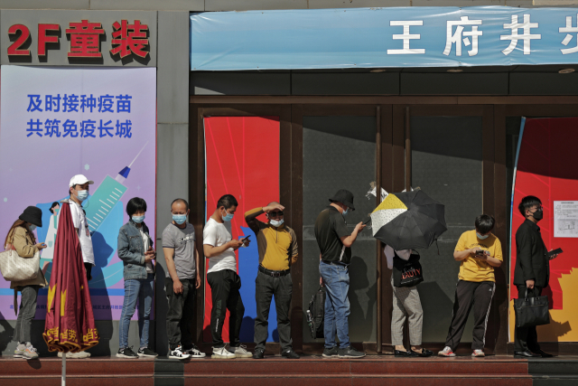 지난 17일 중국 베이징의 한 코로나19 백신 접종소에 중국인들이 길게 줄을 서 있다. 뒤로 간판에 ‘면역 장성을 만들자’는 슬로건이 보인다. /AP연합뉴스