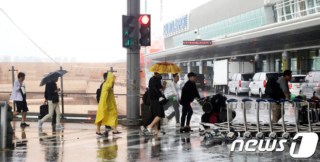 비가 내리고 있는 제주국제공항에서 항공기 이용객들이 우산과 우비를 쓰고 횡단보도를 건너고 있다.© 뉴스1 홍수영 기자