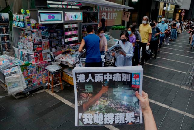 홍콩의 대표적 반중 매체 빈과일보의 폐간 전 '마지막 신문'을 사려는 시민들이 24일 시내 가판대 앞에 길게 줄지어 서 있는 가운데 한 여성이 폐간호 1면을 들어 보이고 있다. 홍콩=AP연합뉴스