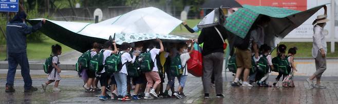 서울의 한 공원으로 나들이를 나온 어린이집 원생들이 교사들과 돗자리로 비를 막으며 이동하고 있다. (이 사진은 기사 내용과 관련 없음) / 연합뉴스