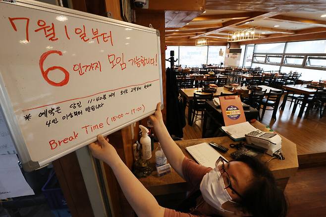 28일 오후 서울시내 한 음식점에서 관계자가 ‘7월1일부터 6인까지 모임 가능’ 안내판을 걸고 있다. 연합뉴스