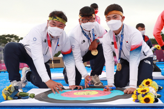 남자양궁대표팀의 오진혁(왼쪽부터), 김우진, 김제덕이 26일 일본 도쿄의 유메노시마공원 양궁장에서 열린 도쿄올림픽 단체전에서 금메달을 획득한 뒤 과녁 점수판에 사인하고 있다. 연합뉴스