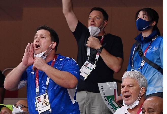Officials from different national teams cheer for their athletes at an Olympic venue in Tokyo with their masks pulled down to their chins on Wednesday. (pool photo)