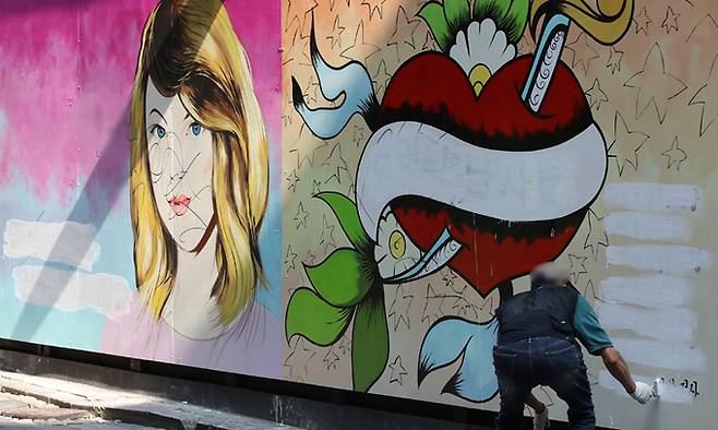 서울 종로구의 한 서점 외벽에 그려진 대권 주자 윤석열 전 검찰총장의 부인 김건희 씨를 비방하는 내용의 벽화가 논란이 되고 있는 가운데 30일 한 건물 관계자가 벽화의 글자를 흰색 페인트로 지우고 있다. 연합뉴스