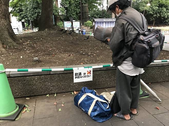 A street person looks at a sign at Ueno Park that says drinking is prohibited at the park. (Lee Jun-hee/The Hankyoreh)