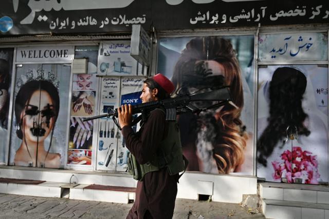 이슬람 무장세력 탈레반에 장악된 아프가니스탄 수도 카불에서 18일 어깨에 소총을 멘 한 탈레반 병사가 여성 모델들의 사진이 훼손된 미용실 앞을 지나고 있다. 카불=AFP 연합뉴스