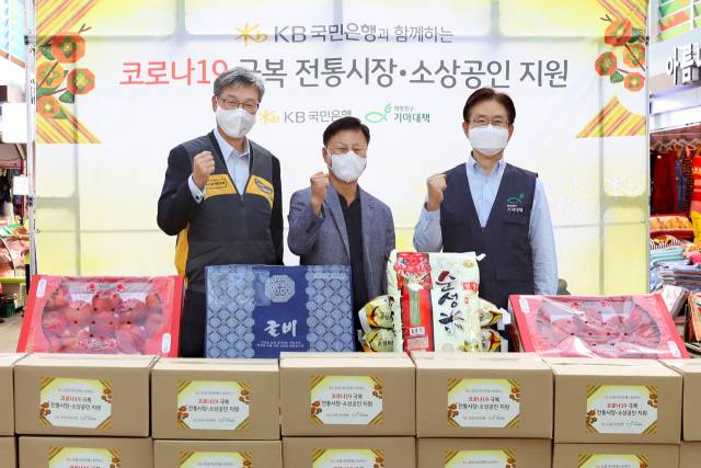 허인(왼쪽부터) KB국민은행장, 김태원 영등포전통시장 상인회장, 유원식 희망친구 기아대책 회장이 15일 서울 영등포시장에서 열린 코로나19 극복 전통시장·소상공인 지원 행사에서 어려운 이웃에게 전달할 쌀·정육·과일 등의 식료품을 구입한 뒤 파이팅을 외치고 있다./사진 제공=국민은행