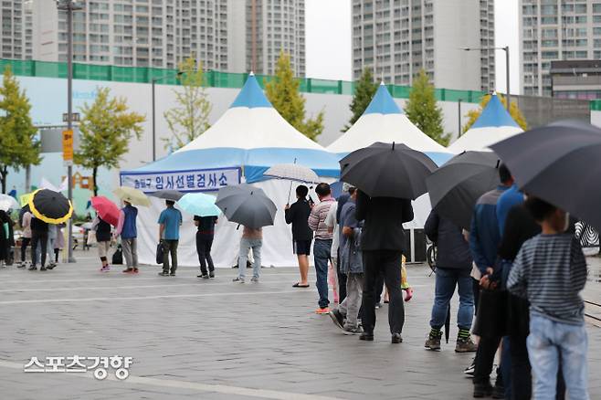 서울 송파구 올림픽공원 임시 선별진료소에서 6일 비가 내리는 가운데 시민들이 코로나19 검사를 받기 위해 줄 서있다. 이날 0시 기준 신규 확진자는 2028명으로 누적 32만3379명이다.  한수빈 기자