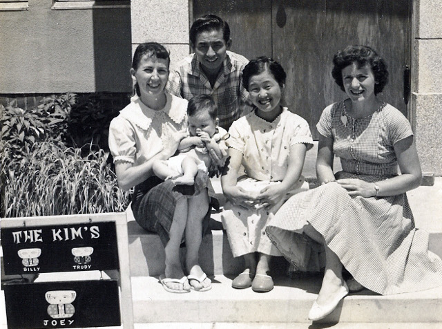 트루디(왼쪽 첫 번째) 사모가 1961년쯤 첫째 아들 김요셉군을 안고 남편 김장환(왼쪽 두 번째) 목사, 지인들과 함께 수원 인계동의 집 문 앞에 앉아서 사진을 찍고 있다. 트루디와 빌리라고 적힌 대문 문패도 세워져있다.