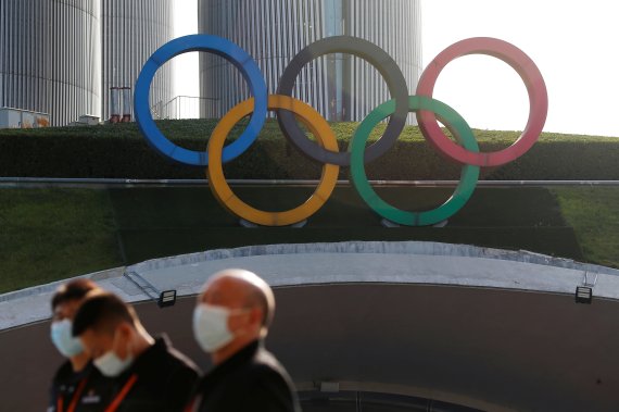 내년 2월 개막하는 베이징동계올림픽을 앞두고 24일 중국 수도 베이징 시내에서 코로나19 확진자가 증가해 비상이 걸렸다. 마스크를 쓴 중국인들이 시내에 걸린 올림픽 휘장 아래를 지나고 있다. 로이터 뉴스1