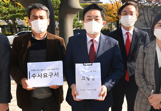 Former Jeju Gov. Won Hee-ryong (right) holds up a criminal complaint against Democratic Party presidential candidate Lee Jae-myung as he makes his way to the Supreme Prosecutors' Office in Seocho district, southern Seoul, on Monday morning. [YONHAP]