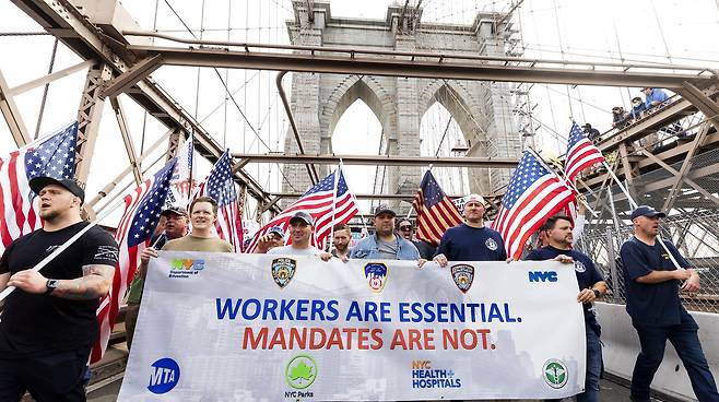 공무원의 백신 접종 의무화에 반대하는 시위대가 25일 뉴욕 브루클린 다리 위에서 가두 시위를 벌이고 있다. '근로자는 필수적이다. 백신 의무화는 그렇지 않다'고 쓴 플래카드를 들고 있다. EPA=연합뉴스