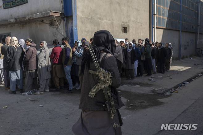 [카불=AP/뉴시스] 지난 17일(현지시간) 아프가니스탄 수도 카불에서 한 탈레반 병사가 유엔 세계식량계획(WFP)이 지급하는 현금을 받기 위해 주민들이 줄 서 있는 거리를 경비하고 있다. 2021.11.21.