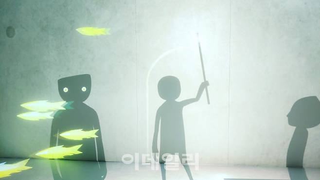 문준용의 미디어아트 ‘어그먼티드 섀도: 별을 쫓는 그림자들’ 중 한 장면. 한 관람객으로부터 작대기 끝에 빛을 받은 한 그림자가 벽에 문을 내고 있다. 그 사이에도 노란 물고기떼는 끝없이 움직인다(사진=오현주 문화전문기자).