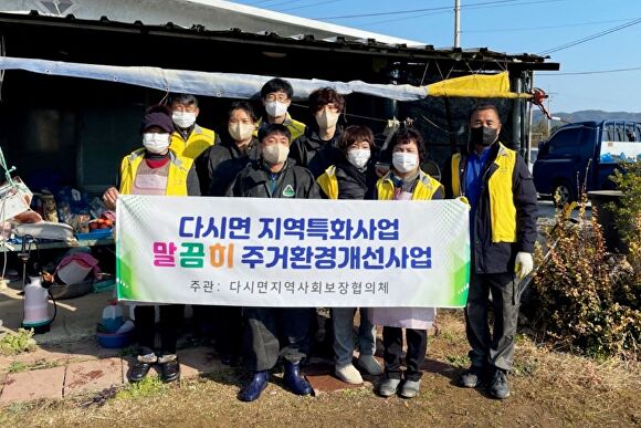 나주시 다시면 지사협 위원들과 청소대행전문업체 푸른세상 직원들이 다시면 주거환경개선사업 관련 현수막을 들고 기념촬영을 하고 있다. [사진=나주시]