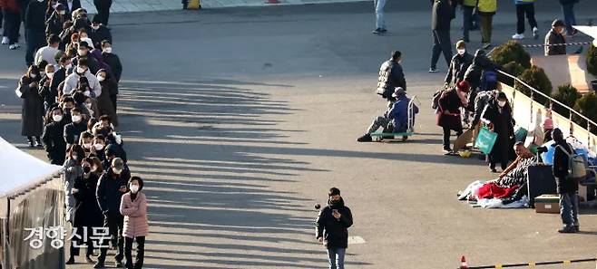 Homeless people (right) watch as citizens line up to get tested at a temporary screening clinic at Seoul Station Square on December 8. Bak Min-gyu, Senior Reporter