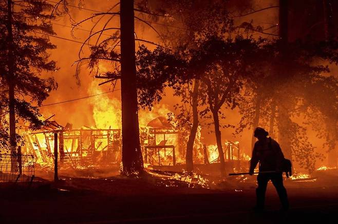 미국 캘리포니아주 플루머스 카운티에서 대형 산불 딕시가 주택을 불태우고 있는 화재 현장을 한 소방관이 지나고 있다. [AP=연합뉴스]
