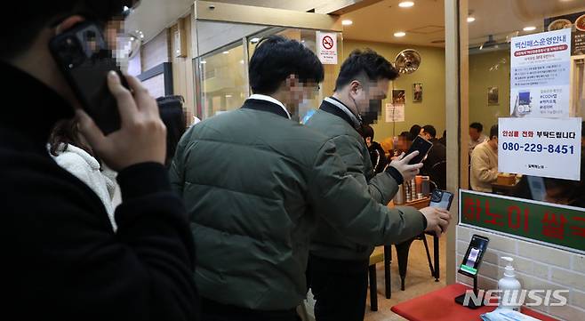 [서울=뉴시스] 이영환 기자 = 방역패스 의무화 시행 이틀째인 14일 서울 시내의 한 식당에서 시민들이 QR코드 인증을 마친 후 식당으로 들어가고 있다. 손영래 중앙사고수습본부(중수본) 사회전략반장은 이날 정례브리핑을 통해 "시스템 과부하 문제로 작동이 원활하지 않은 측면에서의 방역패스 미확인 사례에 대해서는 벌칙 적용을 계속 유예한다"고 밝혔다. 2021.12.14. 20hwan@newsis.com