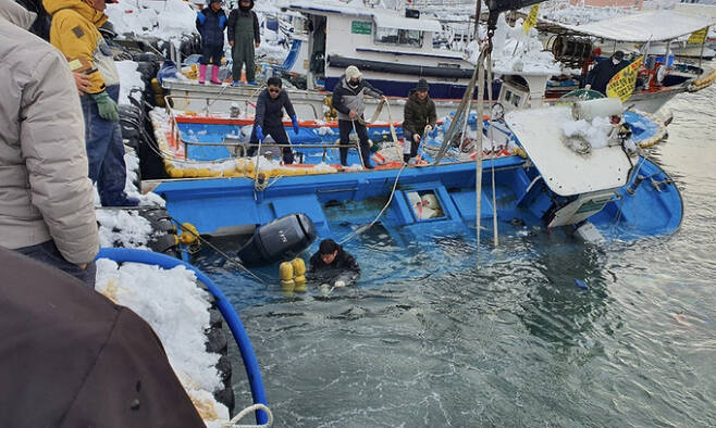 많은 눈이 내린 25일 어업인들과 해양경찰관이 강원도 강릉시 주문진읍 주문진항에서 눈 무게를 이기지 못하고 물에 반쯤 잠긴 어선이 침몰하지 않도록 작업을 하고 있다. 속초해양경찰서 제공