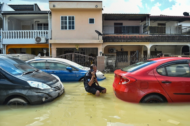 21일(현지시간) 말레이시아 슬랑오르주 샤알람 홍수 지역에서 한 주민이 침수 차량 사이에서 전화를 붙들고 있다./AP연합뉴스