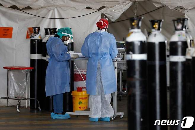 남아공 프리토리아 스티브 비코 아카데믹 병원 임시병동의 빈 산소 탱크 옆에 개인보호장비(PPE)를 착용한 의료 종사자들이 서 있다. © AFP=뉴스1