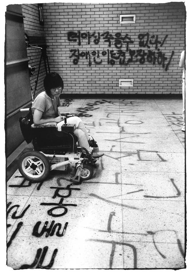 2001년 서울역 역사에 스프레이로 ‘더 이상 죽을 수 없다’는 문구가 적혔다. 장애인 활동가가 바닥을 바라보고 있다. 서울역에서도 2006년 휠체어 리프트 추락으로 장애인이 부상당하는 사고가 일어났다. 사진=차진호