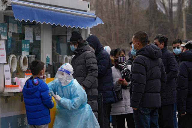 19일 중국 베이징의 임시 신종 코로나바이러스 감염증(코로나19) 검사소 앞에서 주민들이 줄을 선 가운데 한 소년이 코로나19 검사를 위해 검체 채취를 받고 있다. 베이징=AP 연합뉴스