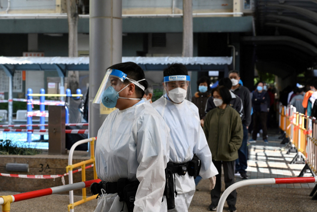 27일(현지시간) 방역복을 입은 홍콩 보건 당국 관계자들 뒤로 홍콩 한 지역 거주자들이 코로나19 검사를 받기 위해 줄을 서 있다. /AFP연합뉴스