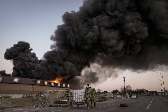 우크라이나 장병들이 키이우 북방에서 불타고 있는 창고 앞을 지나고 있다. AP 통신