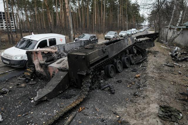 우크라이나 키이우 외곽에서 9일 파괴된 러시아군의 탱크 옆으로 피란 차량들이 빠르게 지나고 있다. 키이우=AP 연합뉴스